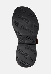 Den svarta gummisulan har en präglad "CAMPER"-logotyp och en textur för grepp. Designen är platt med ett urtag nära hälen.
