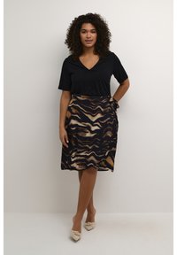 Blusa negra de manga corta combinada con una falda envolvente de colores marrón, marino y crema con un patrón. Tela suave con diseños ondulados, atada en la cintura.