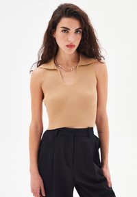 Top senza maniche rigato, color beige, con scollo a V e colletto, abbinato a pantaloni neri a vita alta. Una collana con catena dorata completa l'outfit.