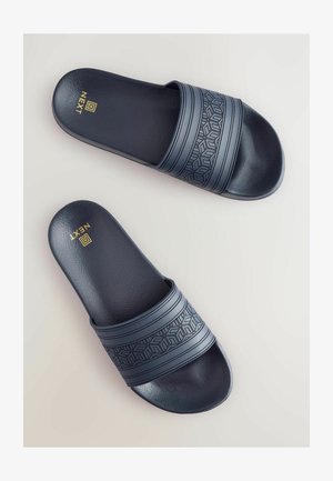 Jūros mėlynos spalvos šlepetės su tekstūruotais dirželiais; turi geometrinį raštą ir lygų gumos paviršių; ant pado įspaustas auksinis logotipas.