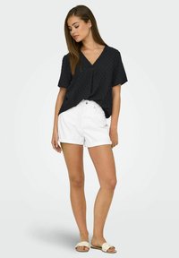 Svart kortärmad topp med strukturerad mönster och V-ringning. Kombinerad med vita rullade shorts och ljusa sandaler. Minimalistisk stil.