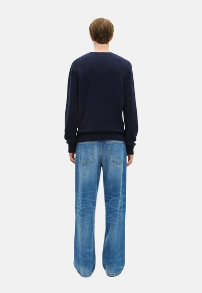 Maglione lavorato a maglia di colore blu navy e jeans in denim a gamba larga di colore blu chiaro. Il maglione ha polsini e orlo a coste; i jeans presentano tasche posteriori e una finitura sbiadita.