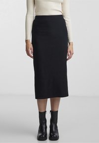 Jupe midi noire côtelée avec une taille ajustée, ornée de rayures verticales, associée à des bottines noires. Présentée sur un fond neutre.
