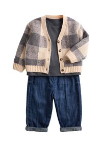 Creme- und grauen karierter Cardigan mit sechs Knöpfen, kombiniert mit einem dunkelgrauen T-Shirt und hochgekrempelten dunkelblauen Jeans.