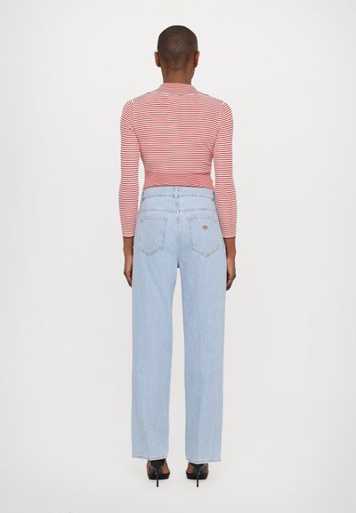 Haut à rayures rouges et blanches, à manches longues, associé à un jean taille haute à jambes larges de couleur bleu clair. Poches arrière visibles et design simple.