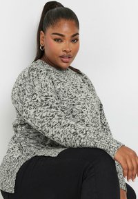 Texturerad stickad tröja i grått och svart med rundad halsringning, sidosprund och ribbade mudd, kombinerad med svarta byxor.