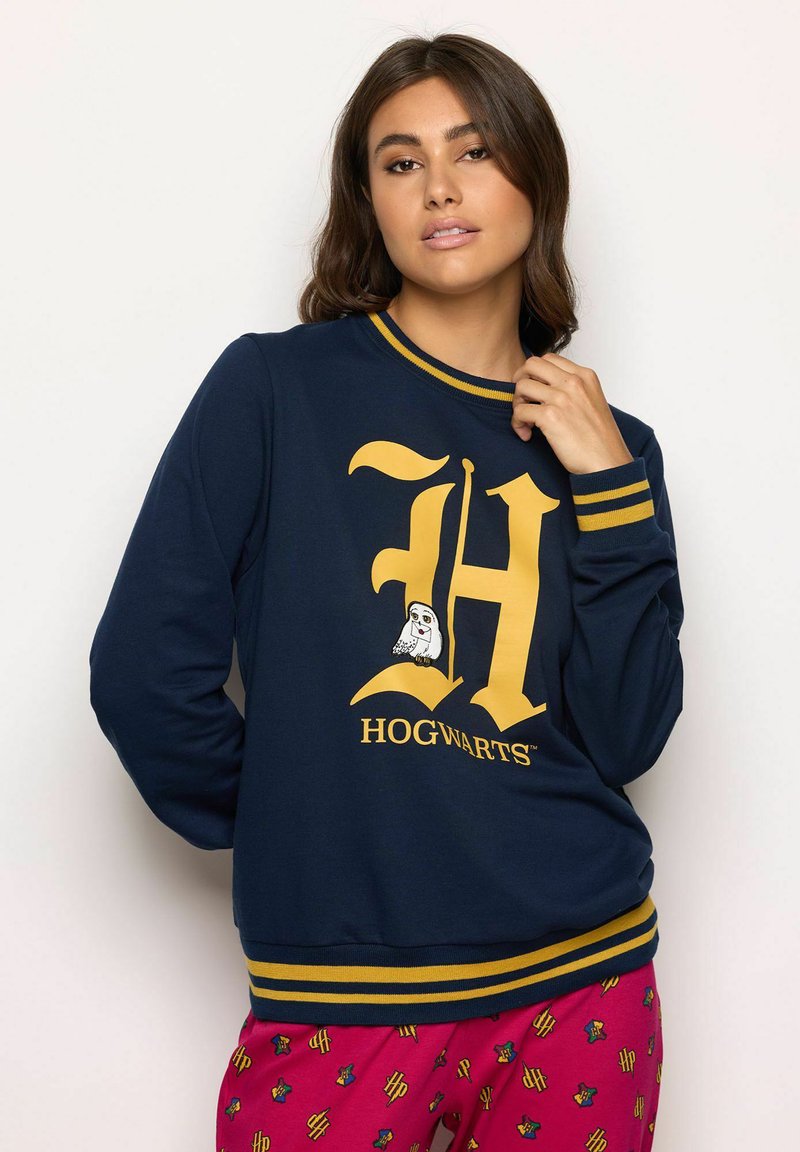 Sudadera blu navy con una grande "H" gialla e il testo "HOGWARTS"; polsini a strisce giallo e blu. Dettaglio grafico di un gufo nel logo.