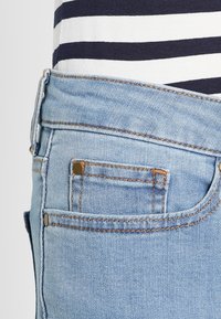 Jeans de mezclilla en un azul claro que presentan un bolsillo trasero con un toque de botón dorado, detalles de costura y una textura ligeramente desgastada.