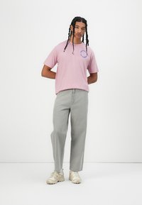 Light pink cotton t-shirt with a round neck and blue graphic text, paired with light gray straight-leg pants and beige sneakers.