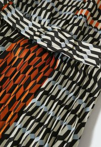 Tissu à motifs géométriques noir, blanc et orange avec des plis et une ceinture assortie dotée d'une boucle circulaire.