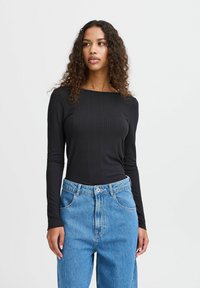 Black ribbed long-sleeve top with a square neckline, paired with high-waisted light blue jeans featuring a button closure and front pockets.