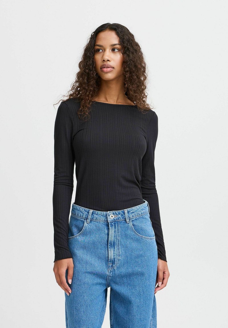 Black ribbed long-sleeve top with a square neckline, paired with high-waisted light blue jeans featuring a button closure and front pockets.