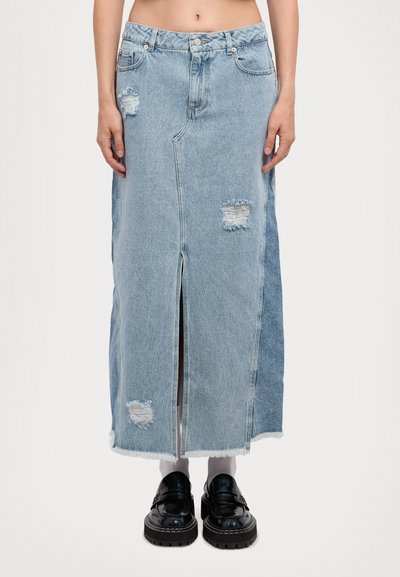 Light blue denim maxi skirt featuring distressed patches, a front slit, and frayed hem. Styled with chunky black shoes and white socks.