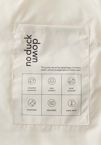 Weißes Jackett mit einem Etikett "kein Gänsedaunen", das Symbole und Text enthält, die die Eigenschaften erläutern: recycelte Isolierung, gemütlicher Komfort, winddicht, atmungsaktiv, verstellbar, super warm.