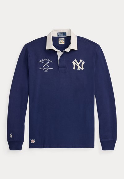 Tengerészkék, hosszú ujjú rögbimez fehér gallérral, New York Yankees logóval, keresztbe tett ütőkkel és Polo Ralph Lauren márkajelzéssel.