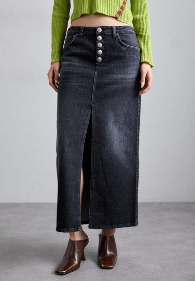 Gonna lunga in denim nera con spacco frontale e chiusura a cinque bottoni. Presenta un taglio classico e una leggera sfumatura, abbinata a stivaletti alla caviglia con tacco marroni.
