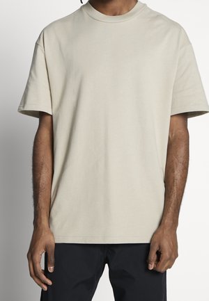 Beżowy, oversize'owy bawełniany t-shirt z krótkimi rękawami, okrągłym dekoltem i gładką teksturą; luźny krój, bez widocznych wzorów czy dodatków.