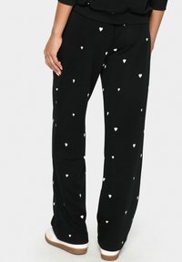 Schwarze Sweatpants aus weichem Stoff, mit verstreuten kleinen weißen Herzmustern. Weit geschnitten mit einem elastischen Bund.