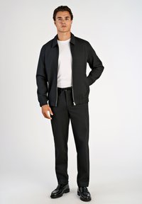 Zwart jasje met rits en een kraag, gedragen over een wit T-shirt. Gecombineerd met zwarte broek en glanzende zwarte nette schoenen. Eenvoudig ontwerp.