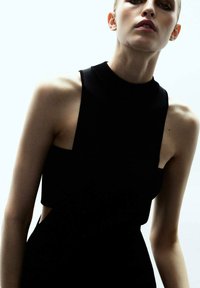 Czarna sukienka bez rękawów z wysokim dekoltem, z wycięciami po bokach. Wykonana z gładkiego, lekkiego materiału o dopasowanym kroju.