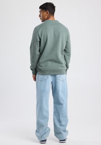 Green cotton sweatshirt with ribbed cuffs, paired with light blue wide-leg denim jeans featuring a faded texture and back pockets.