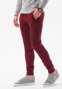 Bordeauxkleurige sweatpants met taps toelopende benen, zijzakken en contrasterende naden, gecombineerd met lichtgrijze sneakers met een gestructureerde afwerking.