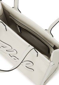 Balts akmens ādas rokassomiņa ar melniem akcentiem, taisnstūra forma, divi rokturi un iekšējais rāvējslēdzēja kabata. Redzama atvērta augšējā daļa.