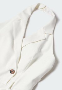 Blouse sans manches blanche avec un col à revers, présentant un détail de bouton marron visible. Le tissu semble lisse avec un léger éclat.