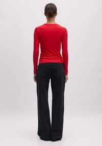 Rotes, geripptes Langarmshirt, kombiniert mit hochgeschnittenen, schwarzen weit geschnittenen Jeans. Das Oberteil hat einen runden Ausschnitt und eine taillierte Silhouette.