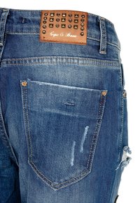 Vaqueros de mezclilla en azul oscuro con detalles desgastados, con un parche de cuero marrón grabado con tachuelas y pequeños acentos de corazón en los bolsillos.
