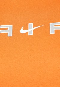 Orange bomull t-shirt med fet vit och grå Nike-logotyp, med en slät och texturerad tygfinish.