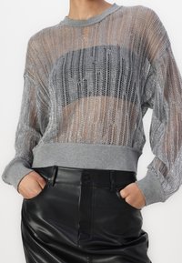 Lekki, srebrny sweter z siateczki o luźnym kroju, z szarymi prążkowanymi mankietami i paskiem na dole. Noszony na czarnym topie, w połączeniu z czarnymi skórzanymi spodniami.