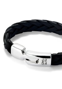 Pulsera trenzada de cuero negro con un cierre de plata con detalles grabados. La textura es suave con un acabado brillante en el herraje.