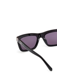 Gafas de sol negras con lentes morados, diseño de montura angular, acentos plateados texturizados en las patillas y brazos curvados y afinados.