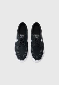 Crne nubuk cipele s bijelim strojem, s bijelim Nike swooshom i ravnim vezicama. Teksturalna površina i minimalistički dizajn.