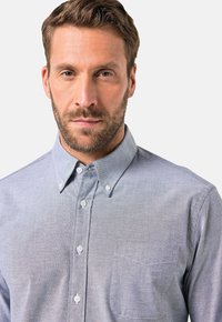 Hellblaues Button-Down-Hemd mit einer Brusttasche, spitzem Kragen und strukturierter Stoffqualität. Weiße Knöpfe ergänzen das Design.