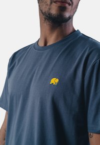 Námořnická modrá bavlněná tričko s kulatým výstřihem, na levé straně hrudi má malou výšivku žlutého slona. Měkká, lehká látka.