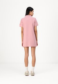 Kort rosa pikétröja med korta ärmar och klassisk krage, som når ovanför mitten av låret. Bärs med ljusa sneakers och ankelstrumpor.