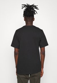 Černé bavlněné tričko s krátkým rukávem, kulatým výstřihem a volným střihem, zobrazené zezadu. Žádné viditelné vzory nebo akcenty.