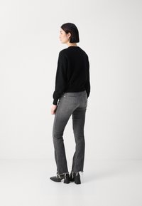 Zwarte trui met een ontspannen pasvorm, grijze high-waisted jeans met rafelige zoom, en zwarte blokhaklaarzen; minimalistisch ontwerp, neutrale kleuren.
