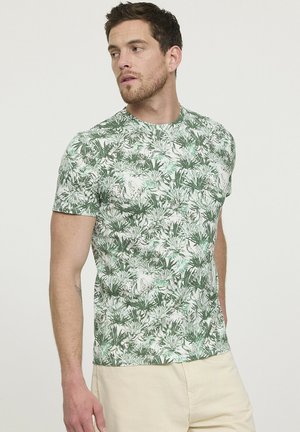 T-shirt en imprimé botanique vert, fabriqué en tissu douce, avec des manches courtes et un col rond. Le motif comprend diverses feuilles vertes sur un fond blanc.