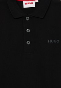 Črna polo majica iz teksturirane tkanine, s tremi sivimi gumbi, ovratnikom in subtilnim črnim logotipom "HUGO" na sprednji strani.