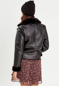 Veste en cuir noir avec un col en fausse fourrure, design court et manches longues ; portée par-dessus une robe florale à motifs et fluide.