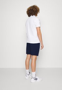 Vit pikétröja, marinblå shorts, vita sneakers med marinblå detaljer. Korta ärmar, avslappnad passform, bakvy, slät tygkänsla.