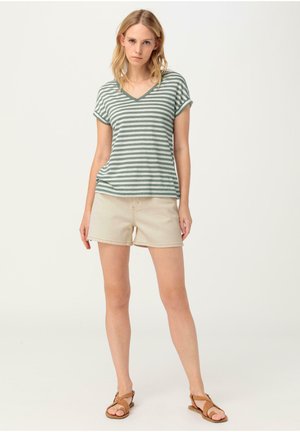 Camiseta de vetéado verde y blanco de cuello en V combinada con pantalones cortos beige. El conjunto presenta mangas cortas y sandalias planas, sobre un fondo neutro.