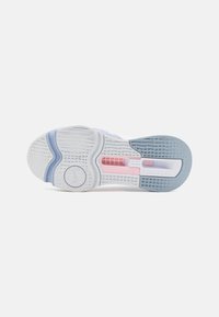 Suela de zapato en goma blanca con acentos en azul y rosa. Superficie texturizada para mayor agarre. Presenta un logo circular y una abertura para flexibilidad.