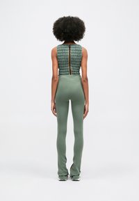 Πράσινο κεντητό αμάνικο τοπ με πίσω φερμο�υάρ και πορτοκαλί λεπτομέρεια. Κουμπωτές πράσινες παντελόνες με φαρδιές άκρες και λεπτομέρεια φερμουάρ στο πλάι.