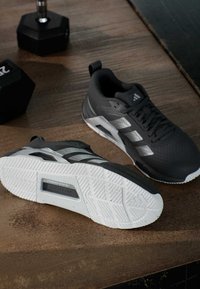 Chaussures de sport noires avec une tige texturée et des accents blancs. Elles présentent une semelle en caoutchouc à motif et des bandes latérales distinctes pour le soutien.