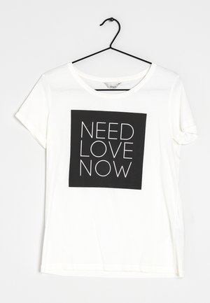 Biała koszulka z krótkim rękawem na czarnym wieszaku, z czarnym kwadratem z przodu z napisem "NEED LOVE NOW" białymi wielkimi literami.