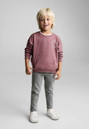 Støvet rosa sweatshirt med hvid grafisk tryk, stor forlomme, parret med grå slim-fit bukser og hvide slip-on sko.